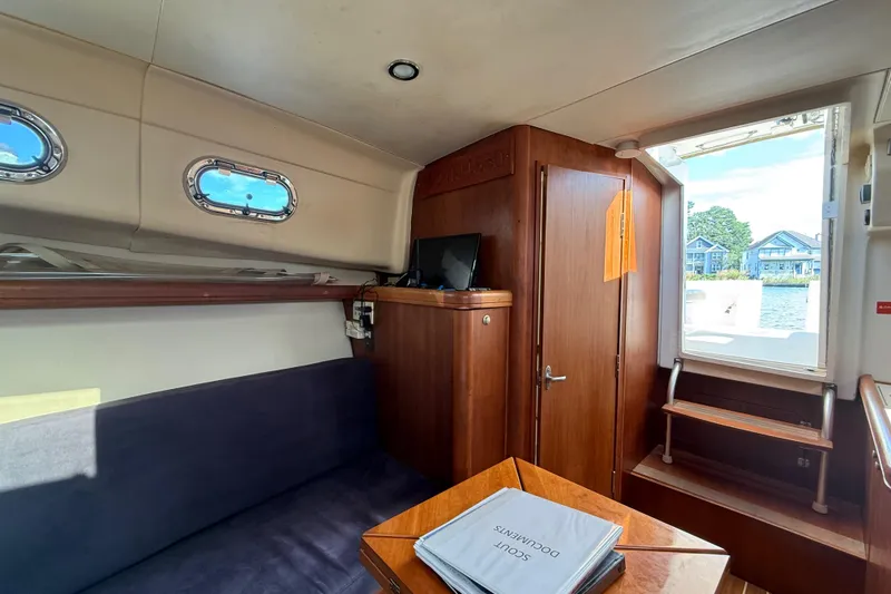Slide: The Image of 2007 Mainship Pilot 30 Sedan interior with seating, wooden cabinetry, and window view. - 19