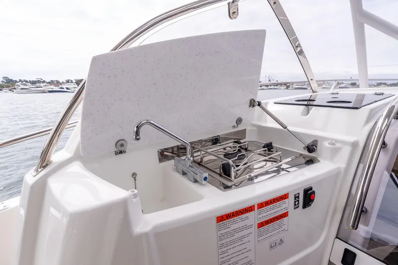 Slide: The Image of 2023 Jeanneau Leader 9.0 WA boat kitchen with stove and sink, docked by the water. - 15