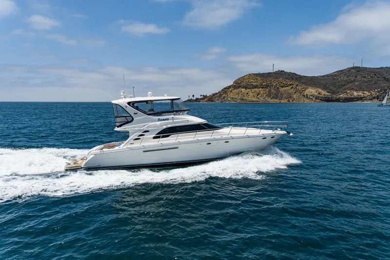 Slide: The Image of 2001 Sea Ray 560 Sedan Bridge yacht cruising on open water near rocky coastline. - 24