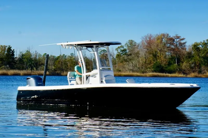 The Image of 2017 Robalo 246 Cayman boat cruising on a calm lake with trees in the background. - 0