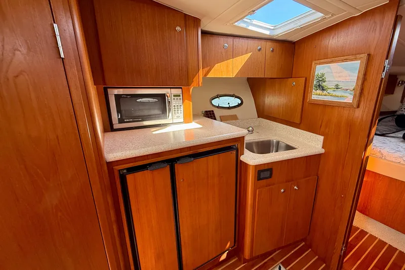 Slide: The Image of 2003 Tiara Yachts 3500 Open interior with kitchenette, featuring microwave, sink, and wooden cabinetry. - 26