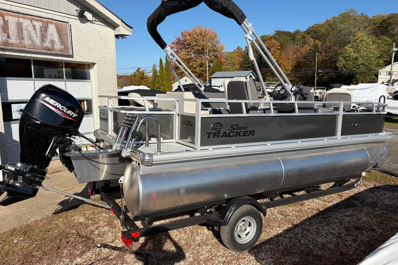 Slide: The Image of 2026 Sun Tracker Bass Buggy 18 DLX pontoon boat with Mercury outboard motor, parked outdoors. - 14