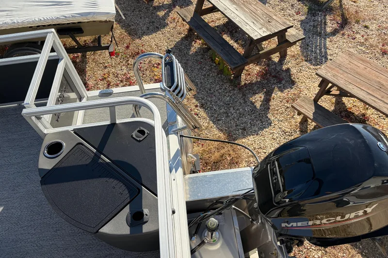 Slide: The Image of 2026 Sun Tracker Bass Buggy 18 DLX pontoon boat with Mercury engine, docked near picnic tables. - 28