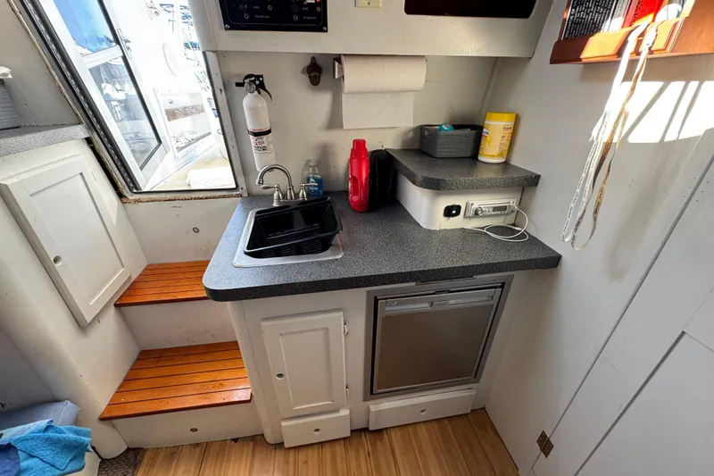 Slide: The Image of Compact kitchen area in a 1986 Luhrs Tournament 290 boat with sink, fridge, and storage. - 24