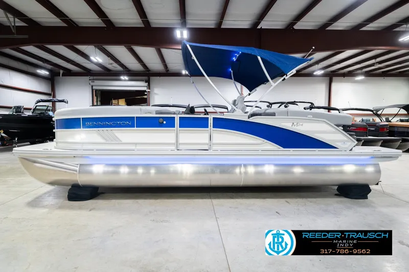 Slide: The Image of 2026 Bennington 24 MOFB pontoon boat with blue accents and canopy in a showroom. - 11