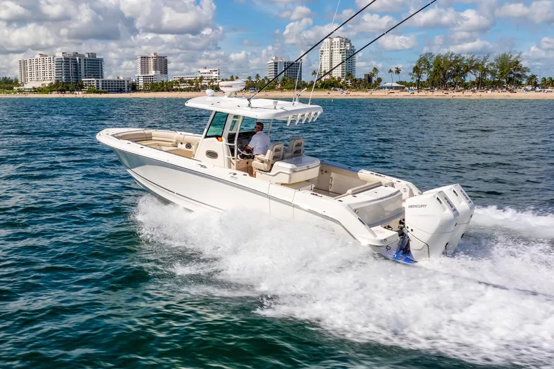 Slide: The Image of 2022 Boston Whaler 330 Outrage cruising near a city shoreline under a partly cloudy sky. - 13