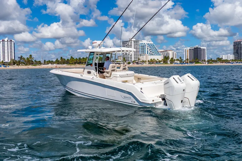 Slide: The Image of 2022 Boston Whaler 330 Outrage boat cruising near a coastal city skyline. - 4