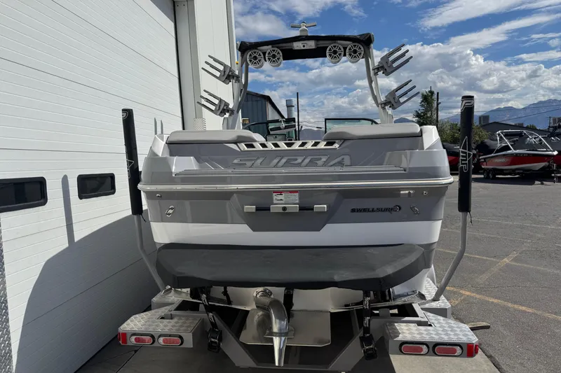 Slide: The Image of 2019 Supra SE 575 boat rear view, parked near a garage under a clear sky. - 3