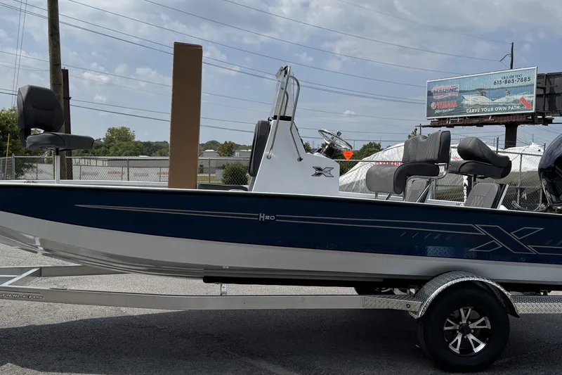 Slide: The Image of 2026 Xpress H20B Bay boat on trailer, blue and white design, parked outdoors. - 9