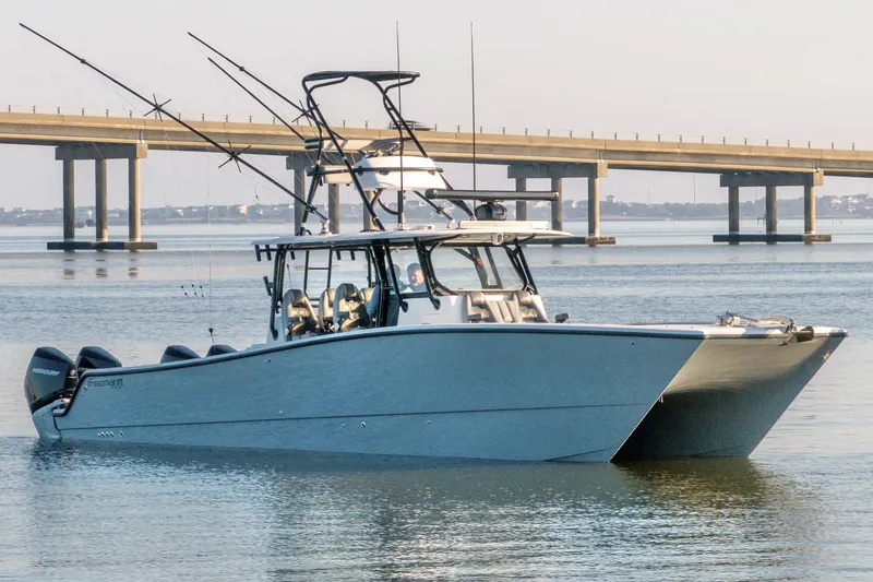 Slide: The Image of 2022 Freeman 42 LR boat on calm water near a bridge, equipped with fishing rods. - 2