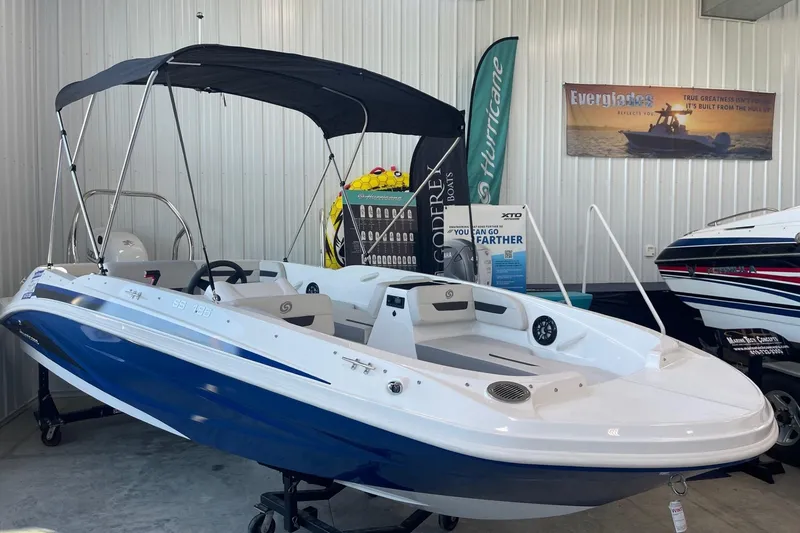 Slide: The Image of 2023 Hurricane SunDeck Sport 185 OB boat displayed indoors with canopy and promotional banners. - 0