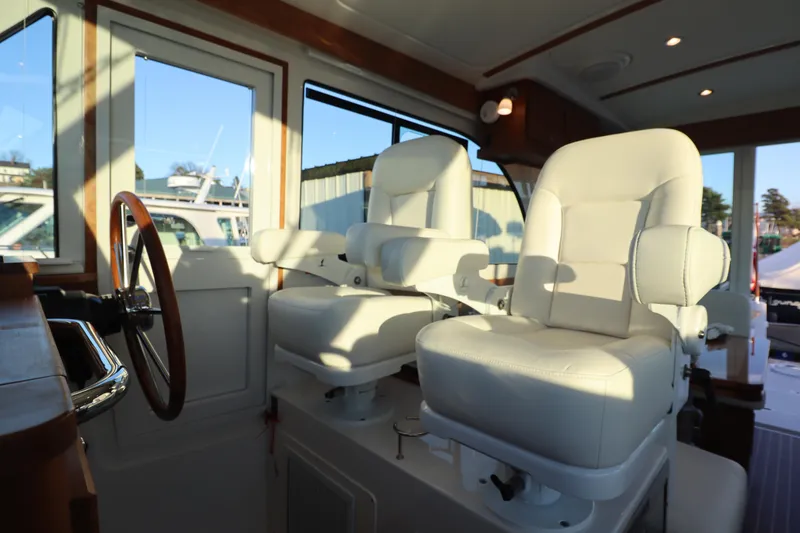 Slide: The Image of Interior of 2026 Back Cove 412 yacht with white captain's chairs and wooden steering wheel. - 12
