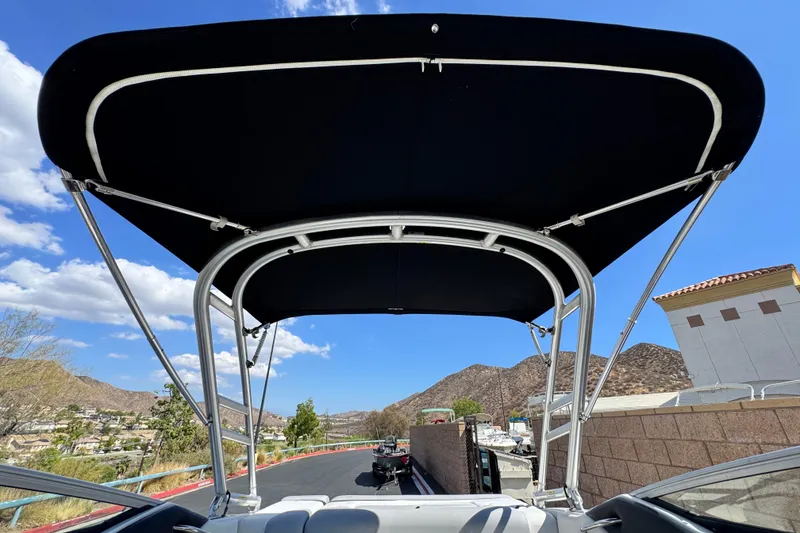 Slide: The Image of 2018 Rinker 23QX BR boat with black bimini top, scenic mountain backdrop. - 10