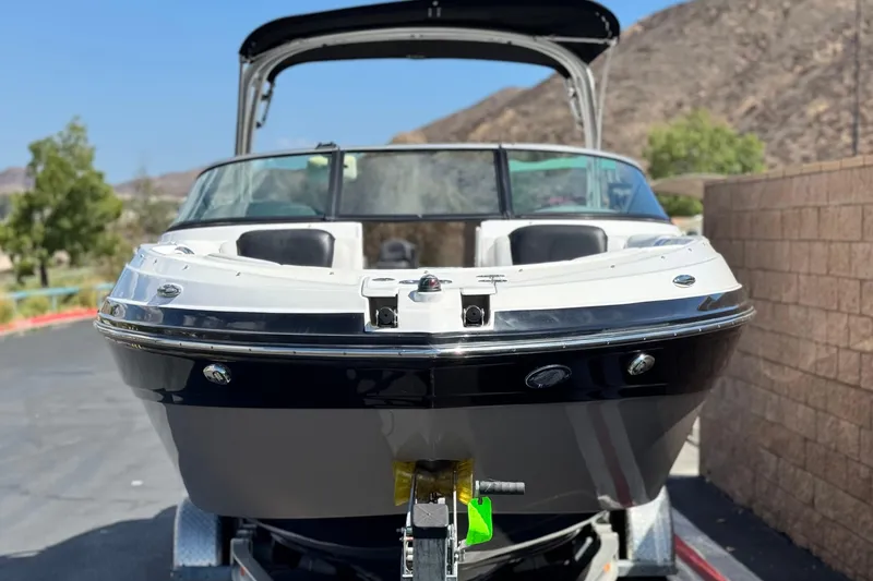 Slide: The Image of 2018 Rinker 23QX BR boat on trailer, parked outdoors with scenic background. - 2