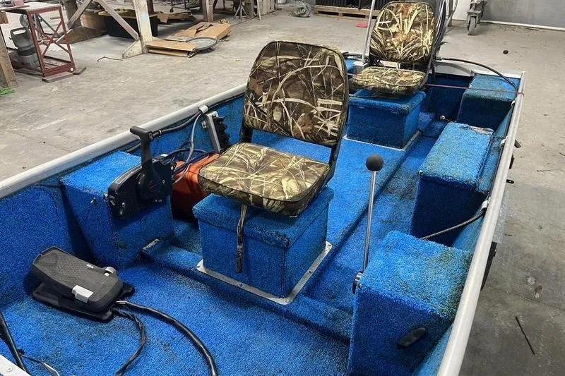 Slide: The Image of 2006 SCANDY WHITE 1310 boat interior with blue carpet and camo seats in a workshop. - 6