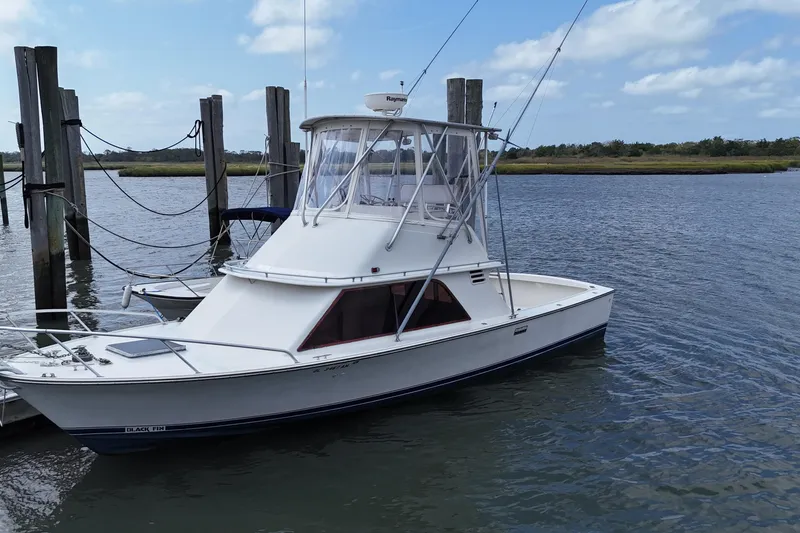 Slide: The Image of 1985 Blackfin 32 Flybridge boat docked on calm water under a blue sky. - 0