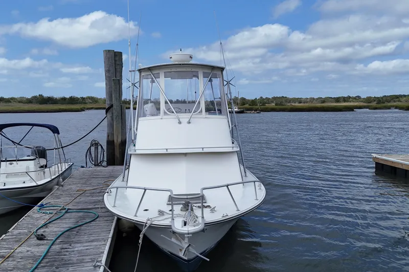 Slide: The Image of 1985 Blackfin 32 Flybridge boat docked on a calm river under a cloudy sky. - 10