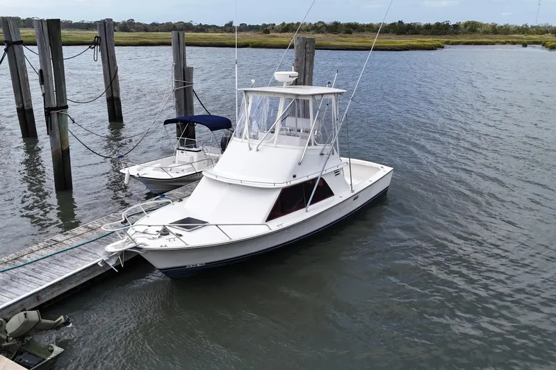 Slide: The Image of 1985 Blackfin 32 Flybridge boat docked on calm water near a wooden pier. - 20