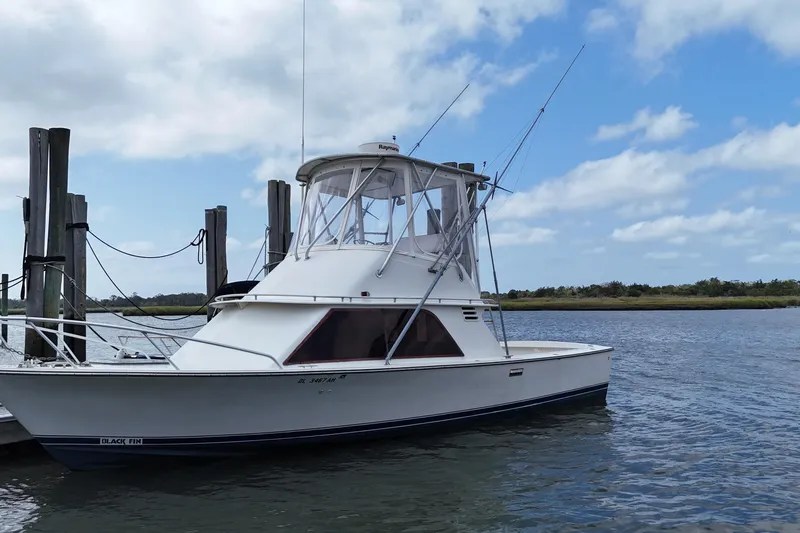 Slide: The Image of 1985 Blackfin 32 Flybridge boat docked on a calm river under a partly cloudy sky. - 9