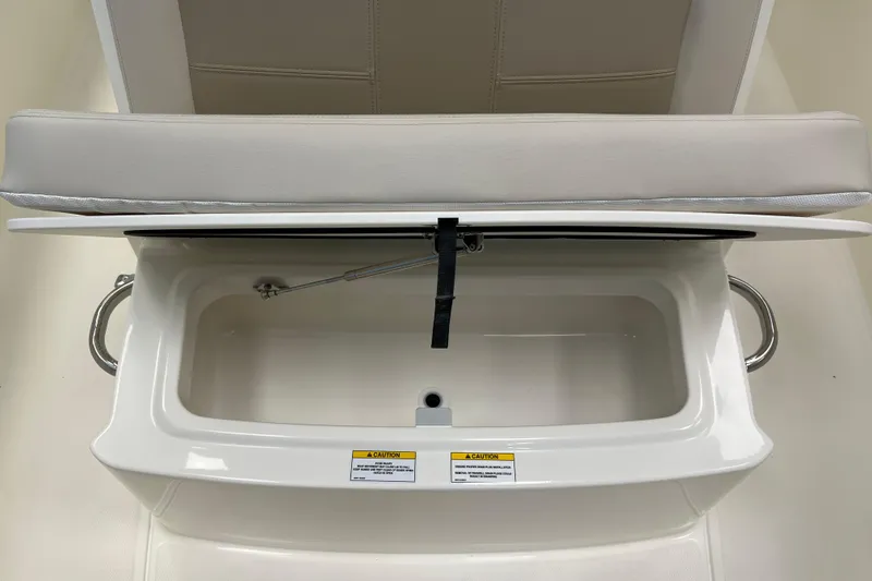 Slide: The Image of 2024 Boston Whaler 230 Outrage storage compartment with cushioned seat and safety warning label. - 22