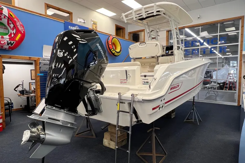 Slide: The Image of 2024 Boston Whaler 230 Outrage boat displayed indoors with Mercury outboard engine. - 4