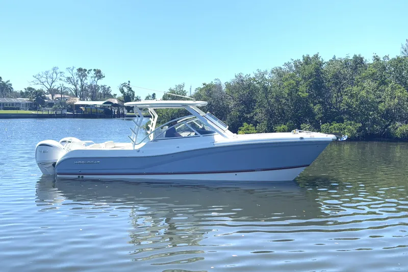 The Image of 2026 World Cat 296 DC boat on calm water, surrounded by lush greenery. - 0