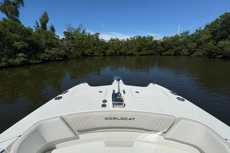 Slide: The Image of Bow view of 2026 World Cat 296 DC boat on calm water, surrounded by lush greenery. - 15