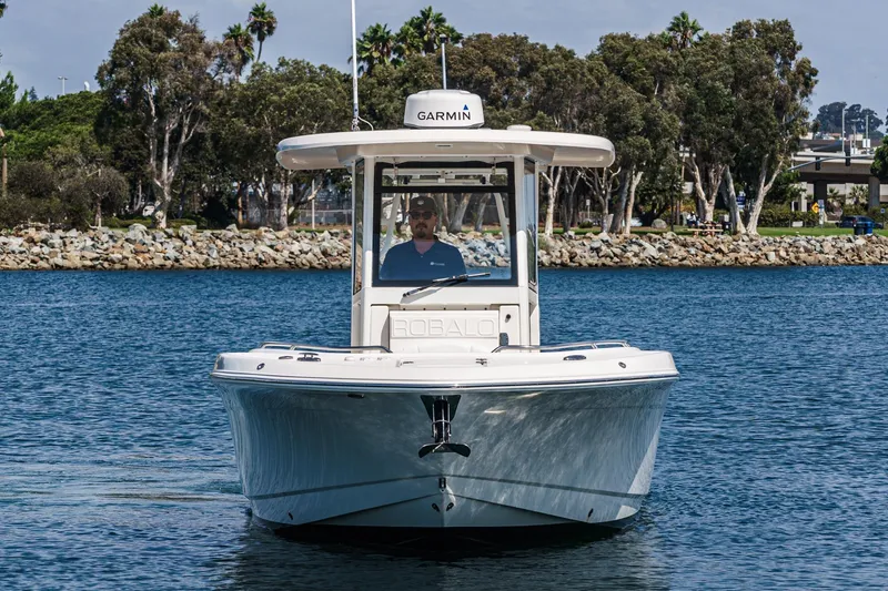 Slide: The Image of 2020 Robalo R272 Center Console boat on water, with Garmin equipment, near rocky shoreline. - 6
