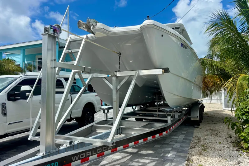 Slide: The Image of 2024 World Cat 325 CC boat on trailer, parked beside a white truck and palm trees. - 10