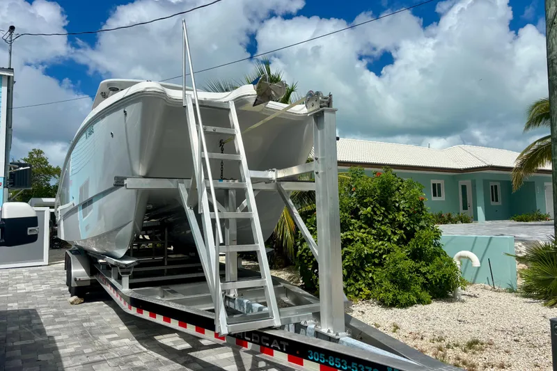 Slide: The Image of 2024 World Cat 325 CC boat on trailer, parked near a house with lush greenery. - 11