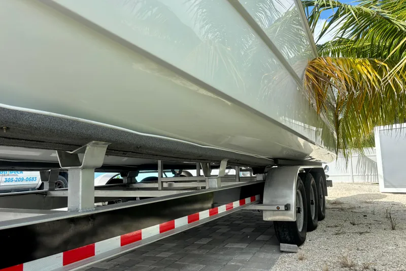 Slide: The Image of 2024 World Cat 325 CC boat on trailer, parked under palm trees. - 14