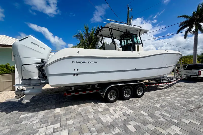 Slide: The Image of 2024 World Cat 325 CC boat on trailer, parked on paved driveway under clear blue sky. - 2