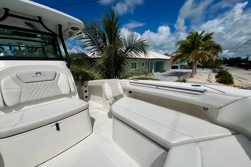 Slide: The Image of 2024 World Cat 325 CC boat interior with white seating, palm trees, and blue sky background. - 24