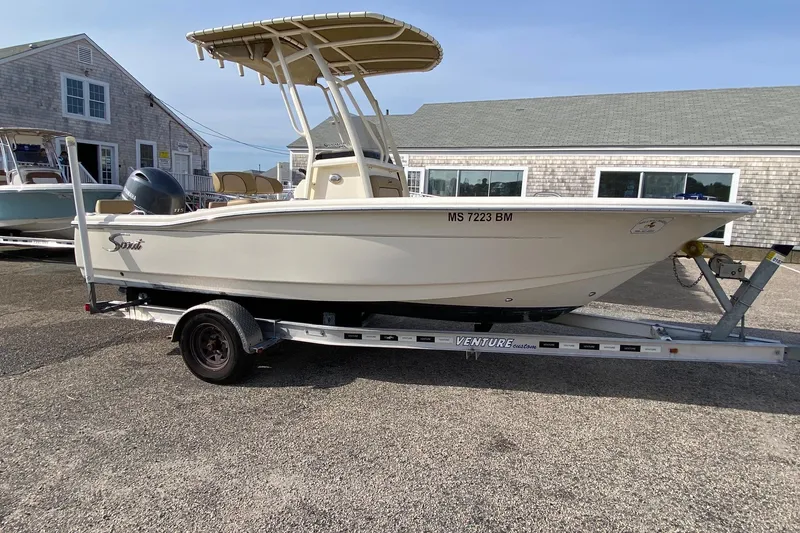 Slide: The Image of 2018 Scout 195 Sportfish boat on trailer, parked near coastal buildings. - 2