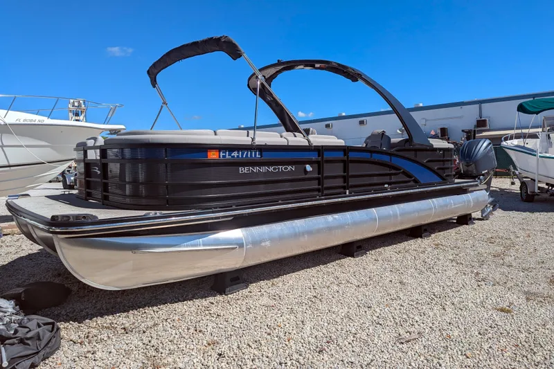 Slide: The Image of 2023 Bennington R 27 RSRAX2 pontoon boat on gravel lot under clear blue sky. - 4