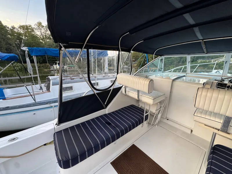 Slide: The Image of 1999 Mainship Pilot 30 Sedan interior with striped seating and canopy, docked near other boats. - 10