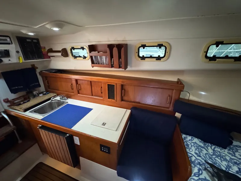 Slide: The Image of 1999 Mainship Pilot 30 Sedan interior with kitchenette, wooden cabinets, and seating area. - 20