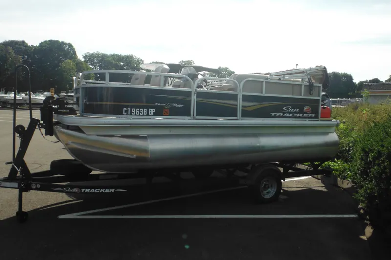 The Image of 2024 Sun Tracker Bass Buggy 16 XL Select pontoon boat on trailer, parked outdoors. - 0