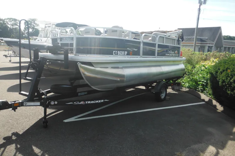 Slide: The Image of 2024 Sun Tracker Bass Buggy 16 XL Select pontoon boat on trailer in parking lot. - 2