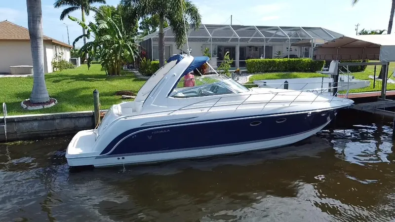 Slide: The Image of 2003 Formula 37PC boat docked near a waterfront home with lush greenery. - 2