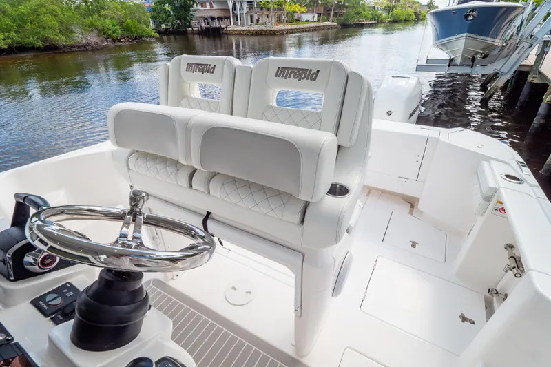 Slide: The Image of 2023 Intrepid 345 Valor boat interior with steering wheel and seating, docked by a scenic waterway. - 82