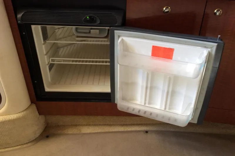 Slide: The Image of Open mini fridge inside 2003 Sea Ray 320 Sundancer boat, showing empty shelves. - 16
