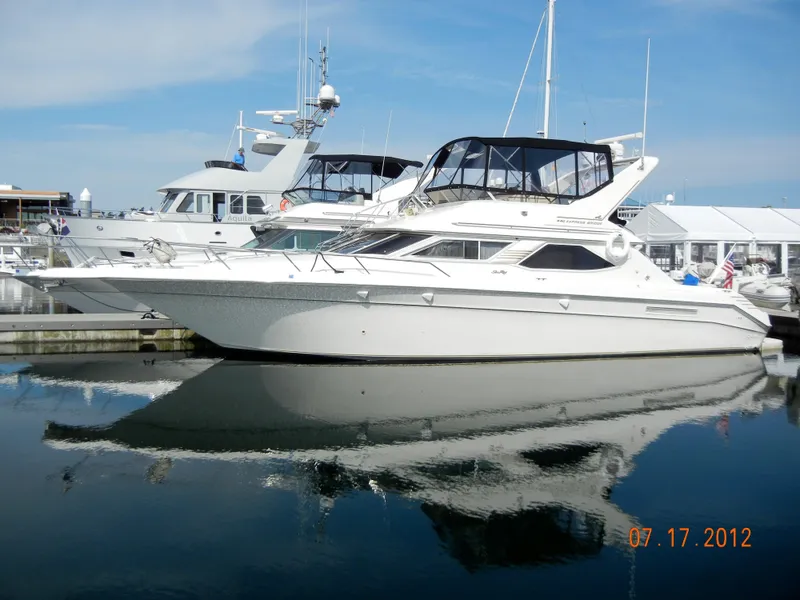 The Image of 1997 Sea Ray 440 Express Bridge yacht docked at marina, reflecting on calm water. - 0