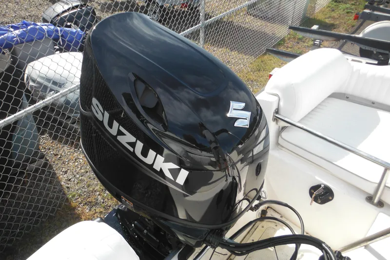 Slide: The Image of 1998 Boston Whaler 20 Ventura Bowrider with Suzuki outboard motor, parked near a chain-link fence. - 34