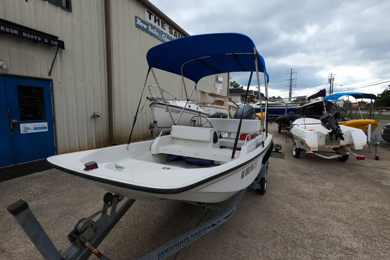 Slide: The Image of 1992 Boston Whaler 13 GLS boat with blue canopy on trailer, parked outside a building. - 10