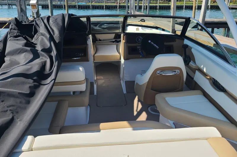 Slide: The Image of 2022 Cobalt CS22 boat interior with beige seating and black cover, docked by the water. - 6