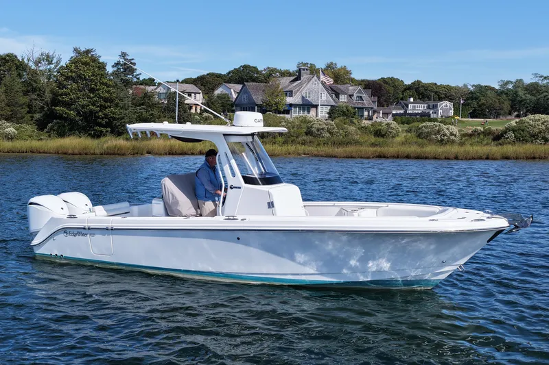 The Image of 2023 Edgewater 262CC boat cruising on a serene lake near waterfront homes. - 0
