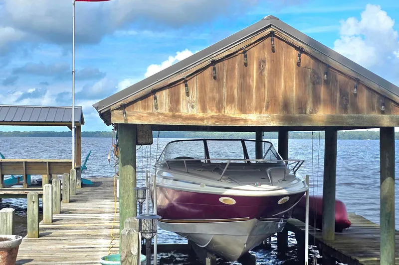 Slide: The Image of 1995 Maxum 2300 SC boat docked under wooden shelter by a lake. - 2