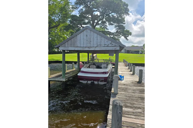 Slide: The Image of 1995 Maxum 2300 SC boat docked under a wooden shelter by a lakeside. - 26