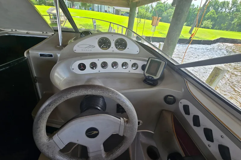 Slide: The Image of 1995 Maxum 2300 SC boat dashboard with steering wheel and gauges, docked by the water. - 7